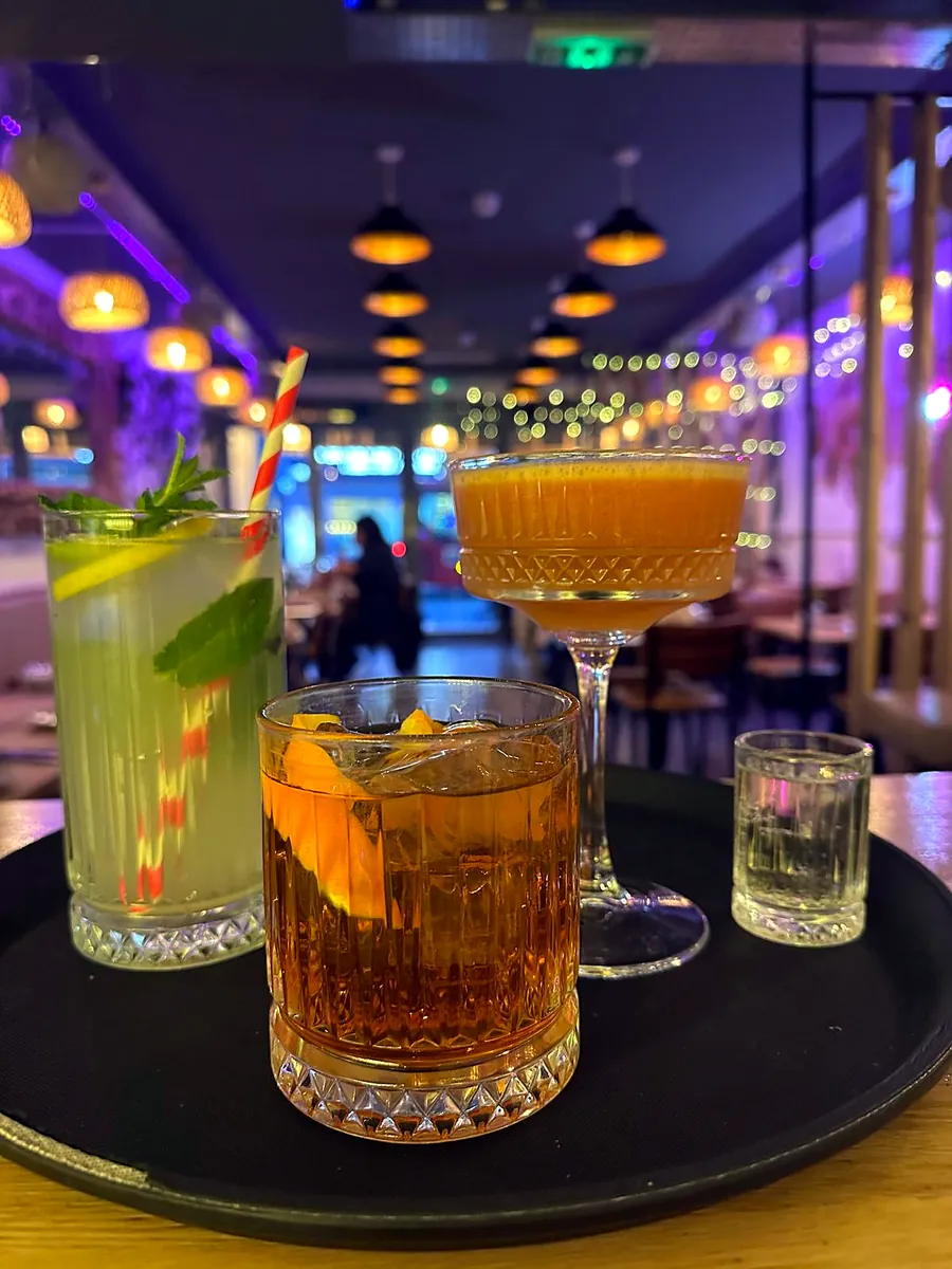 Three cocktails on a tray at the bar, with the dining room behind
