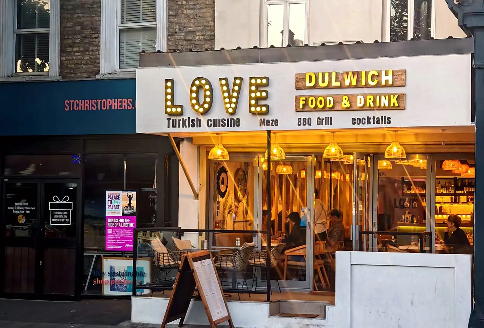 The Love Dulwich shopfront on Lordship Lane at dusk, with its glowing LOVE marquee sign and warm rattan lights inside