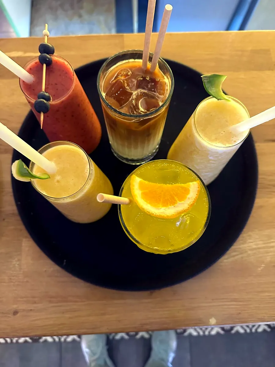 Five smoothies, juices and an iced coffee on a round tray
